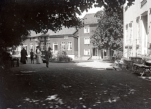 Husen kring Skvallertorget på Gustafsberg innehöll hyresrum. Till höger Hotell Slottet, rakt fram Bikupan och till vänster Tvåan. Foto omkring 1900. UMFA 54477:0172.