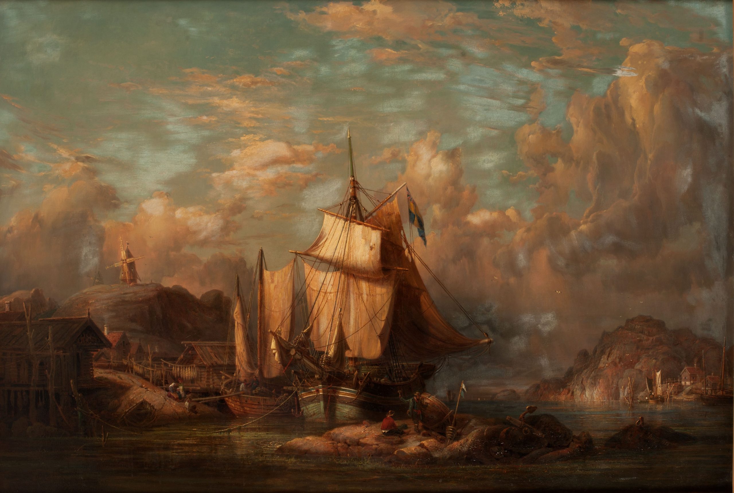 Målning med solnedgång i dramatiska färger. Två fartyg är förtöjda mellan klippor intill fiskeläge med sjöbodar och fisk på tork. På höjden en väderkvarn.
