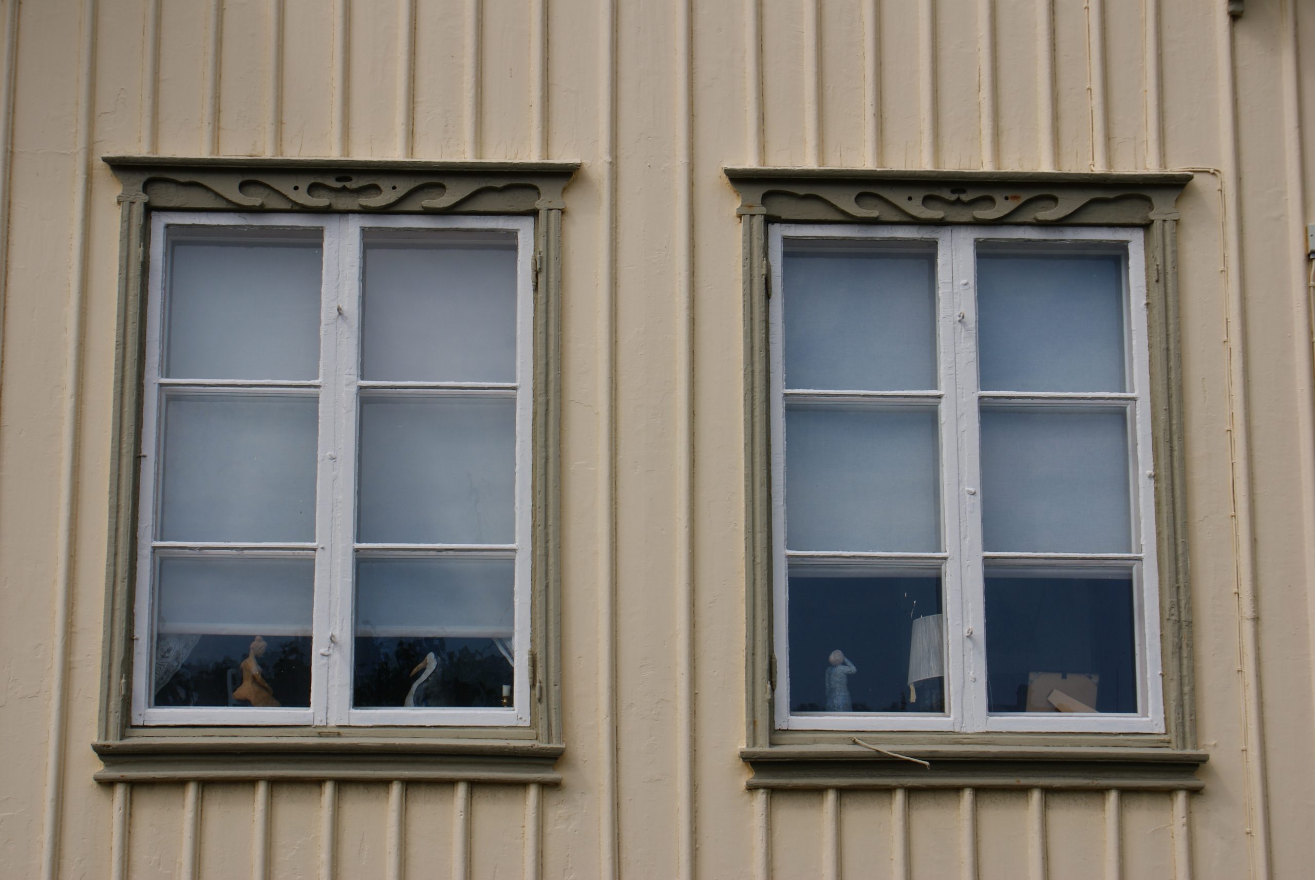 Detaljfoto. En fasad med närbild på två vita sexdelade fönster med grågröna profilerade fönsterfoder.