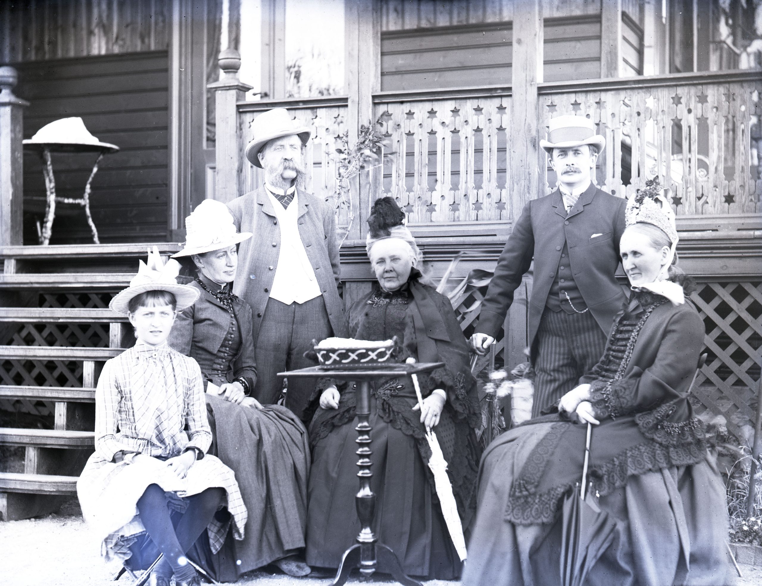 Svartvitt foto. Gruppbild med sex personer runt ett trädgårdsbord.