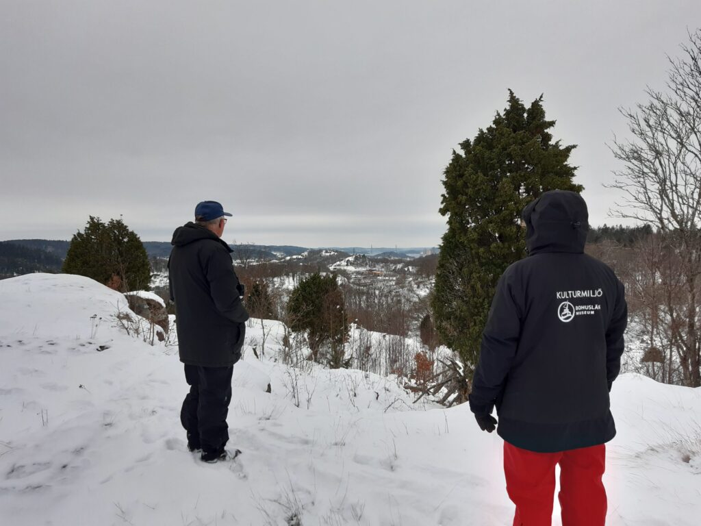 Foto. Två personer i vinterkläder står på ett snötäckt berg.