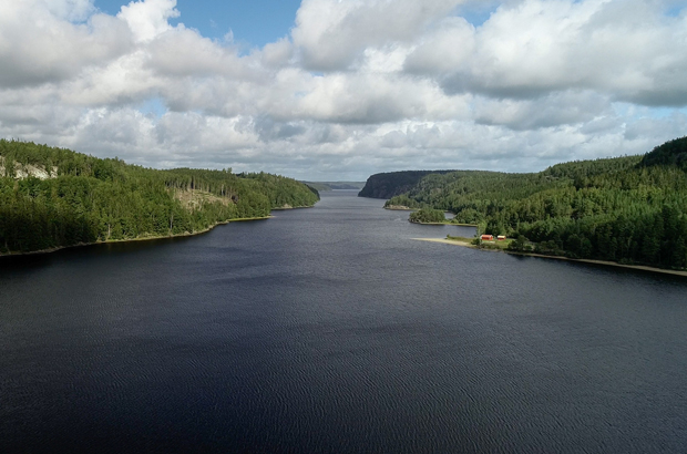 Färgfoto från en höjd över en avsmalnande sjö med berg och skog på sidorna.