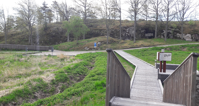 Färgfoto med träramp som leder mot ett berg där en annan ramp leder uppåt.