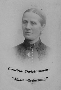 Svartvitt foto. Porträtt av Carolina Christianson i medelåldern. Håret är hårt struket bakåt, ansiktsuttryck och blick är allvarsam.