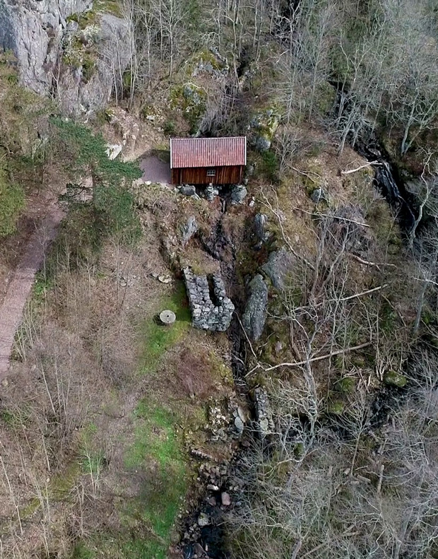 Flygfoto på kvarnbyggnaden som står över en uttorkad bäckfåra i ett bergigt landskap..