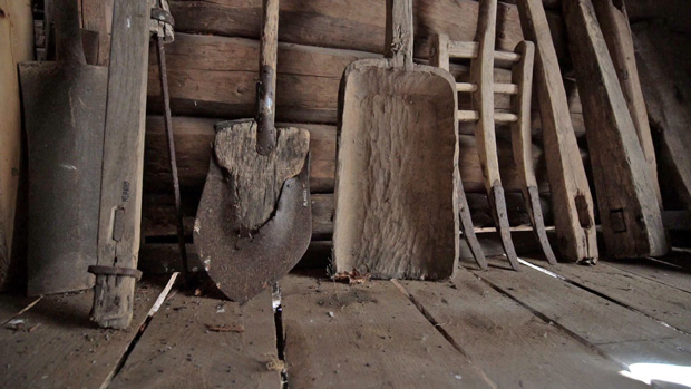 Foto. Redskap lutande mot en kvarnbyggnadens timrade inner-vägg, bland annat en järnskodd spade med träskaft. 