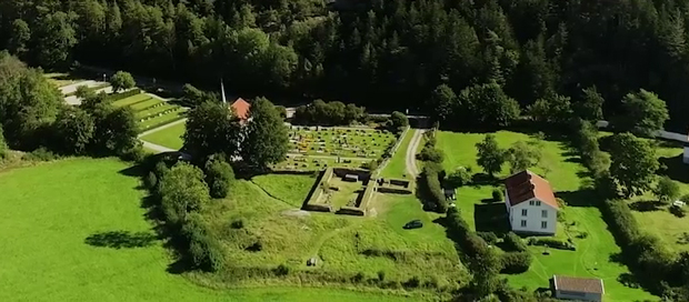 Flygbild i färg, Ruin, kyrkogråd och ett par hus syns på avstånd.