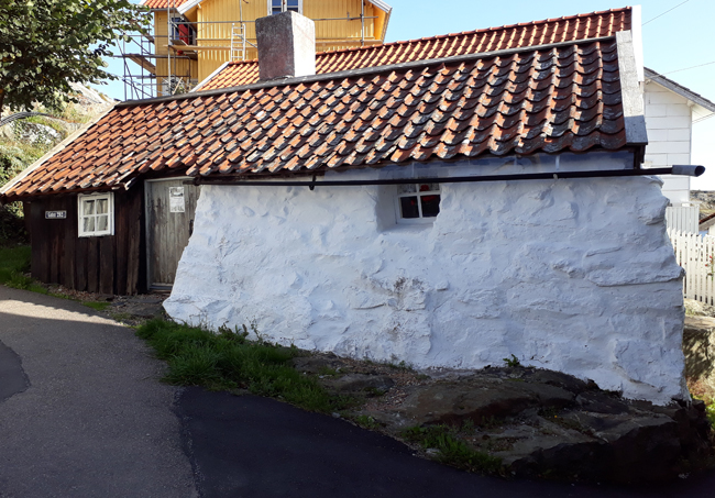 Färgfoto av vitkalkad stenbyggnad med små fönster strax under tegeltaket.