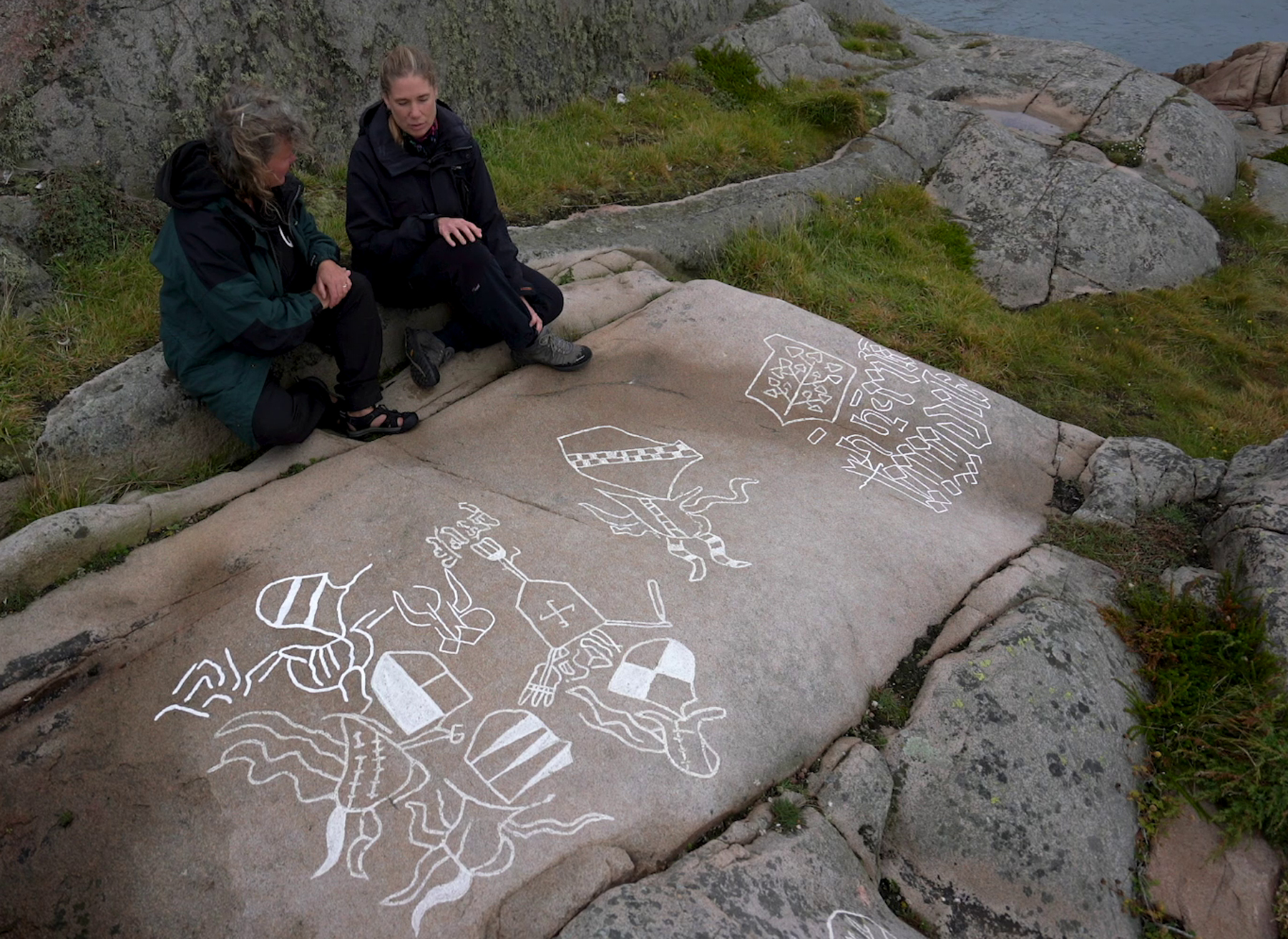 Färgfoto på berghäll och två personer som sitter invid och samtalar