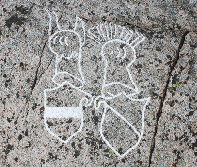 Färgfoto av grå berghäll, fläckvis med svart lava och inristning ifylld med vit färg. med svart 