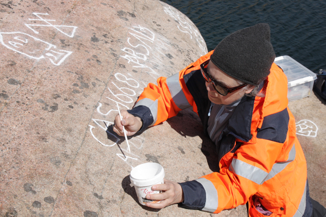 Färgfoto på en kvinna som målar i ristningar med vit färg.