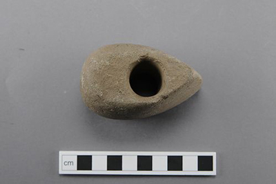 Färgfoto av ett tillspetsat föremål av sten med ett stort hål mitt i.