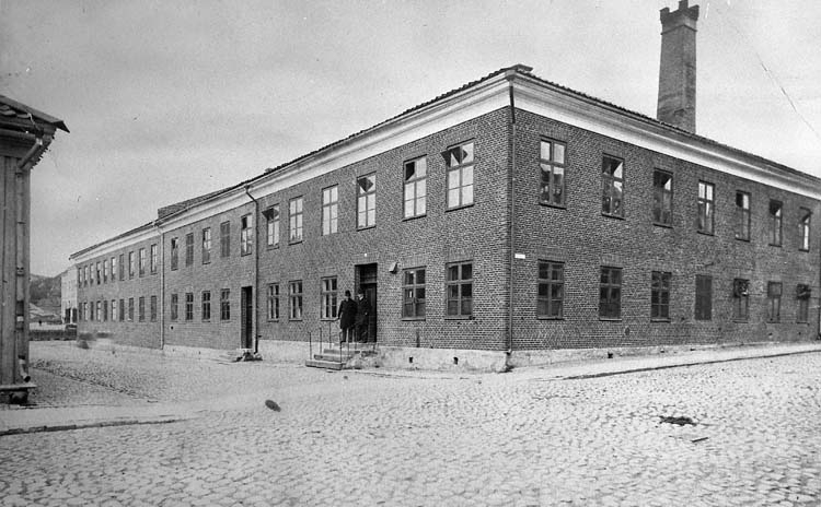 Svartvit foto med en gatukorsning med ett tvåvånings stenhus i tegel.