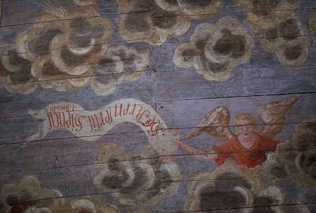 Målat kyrktak med en ängel som håller i ett språkband.