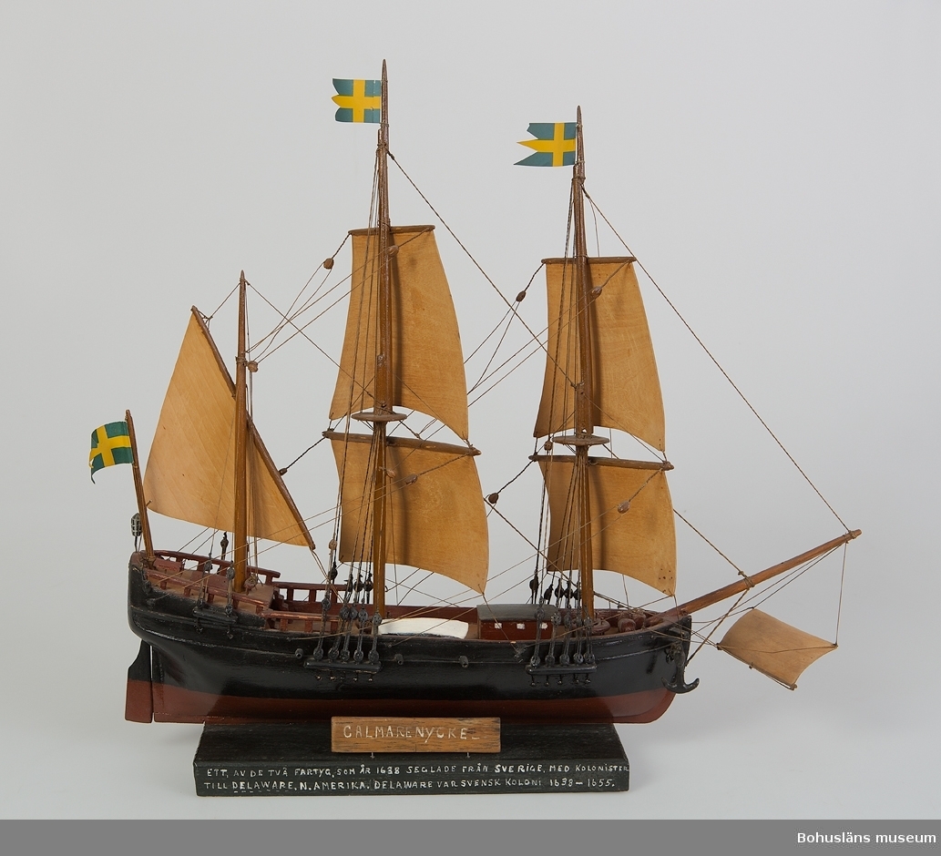 Modell av tremastat skepp med spända segel och flaggor i topp.