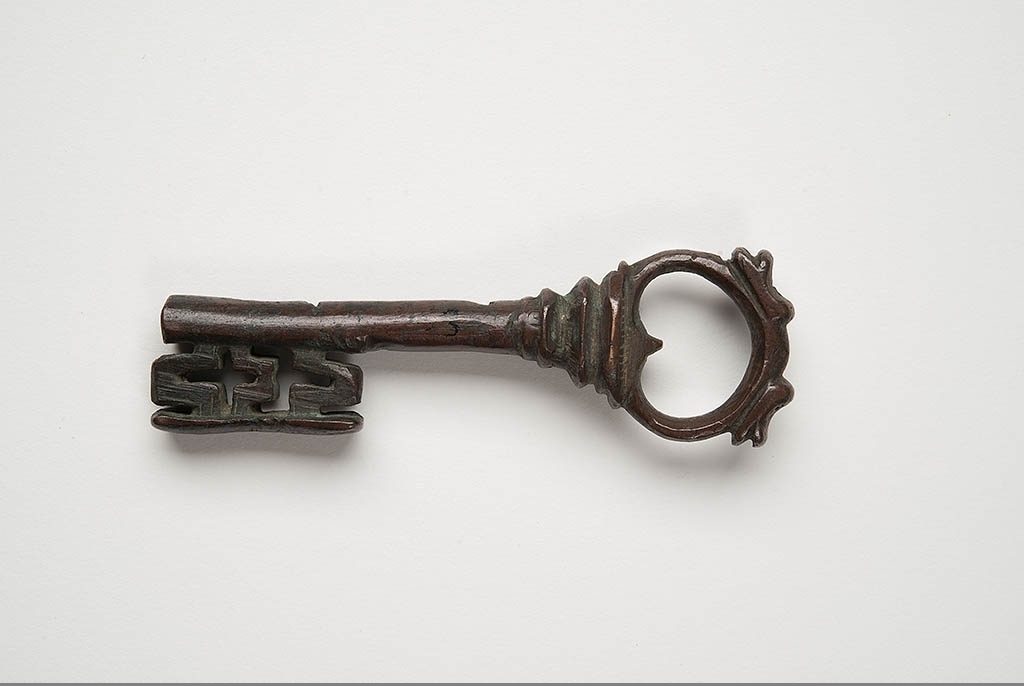 Foto med en 10 cm lång bronsnyckel med dekor av drakhuvuden.