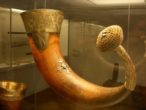 Färgfoto av ett ca 50 centimeter långt uroxehorn med silverbeslag med inristade vapensköldar och avslutas med en rund knopp.