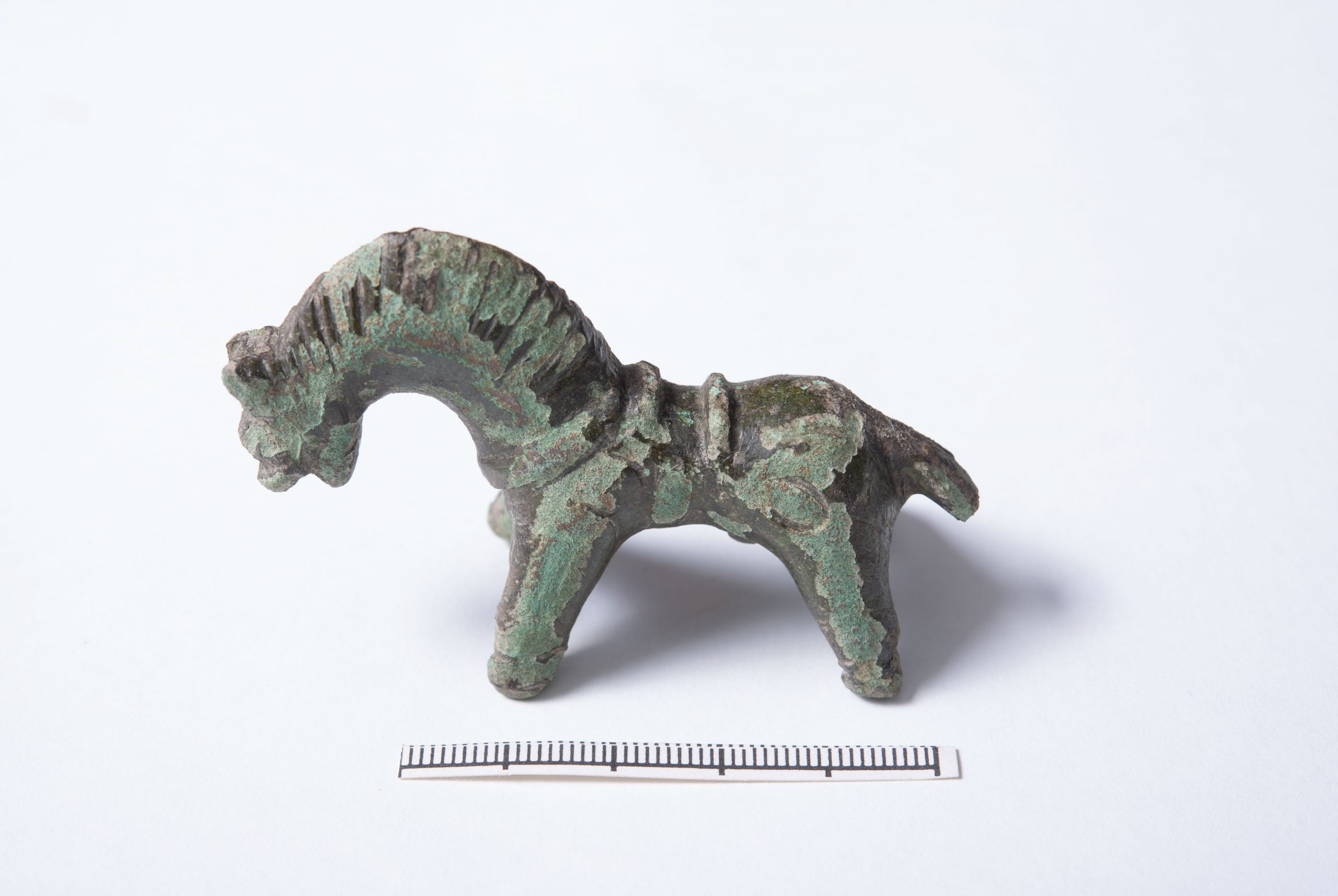 Färgfoto av 7 cm lång bronshäst med sadel.
