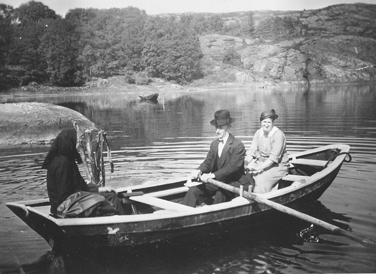 Svartvitt foto med tre personer i en roddbåt. En av kvinnorna är klädd i svart sjalett.