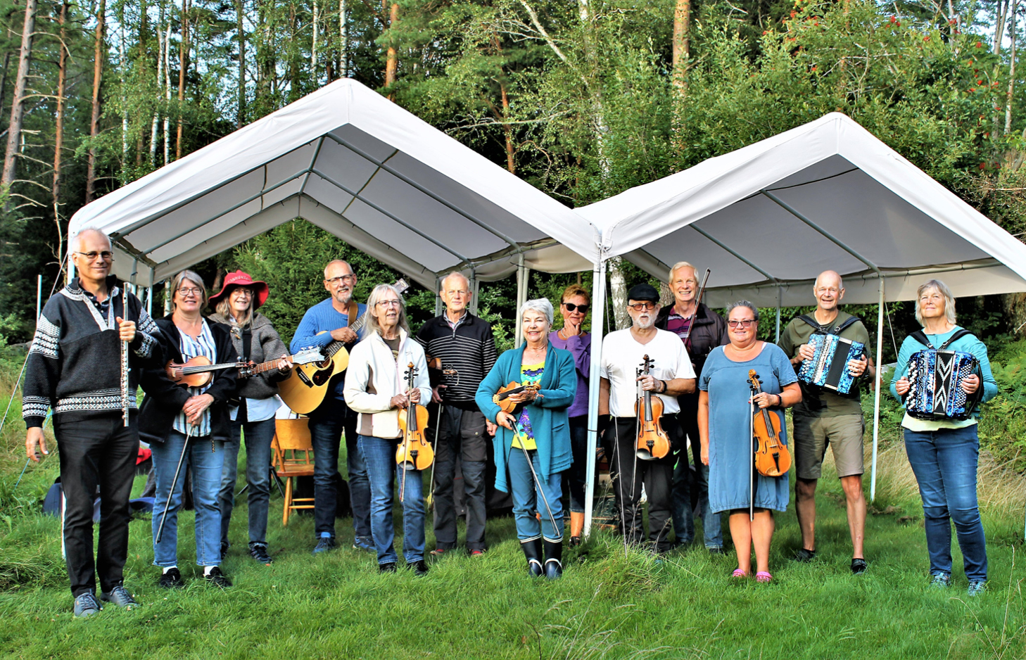 Gruppfoto. Bokenäsets Ådras tretton musiker, utomhus i grönt gräs under två vita partytält