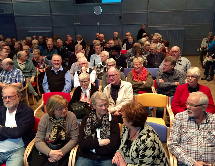 Foto. Sittande publik i en del av Bohusläns museums Hörsal. Ett trettiotal personer i övre medelåldern.
