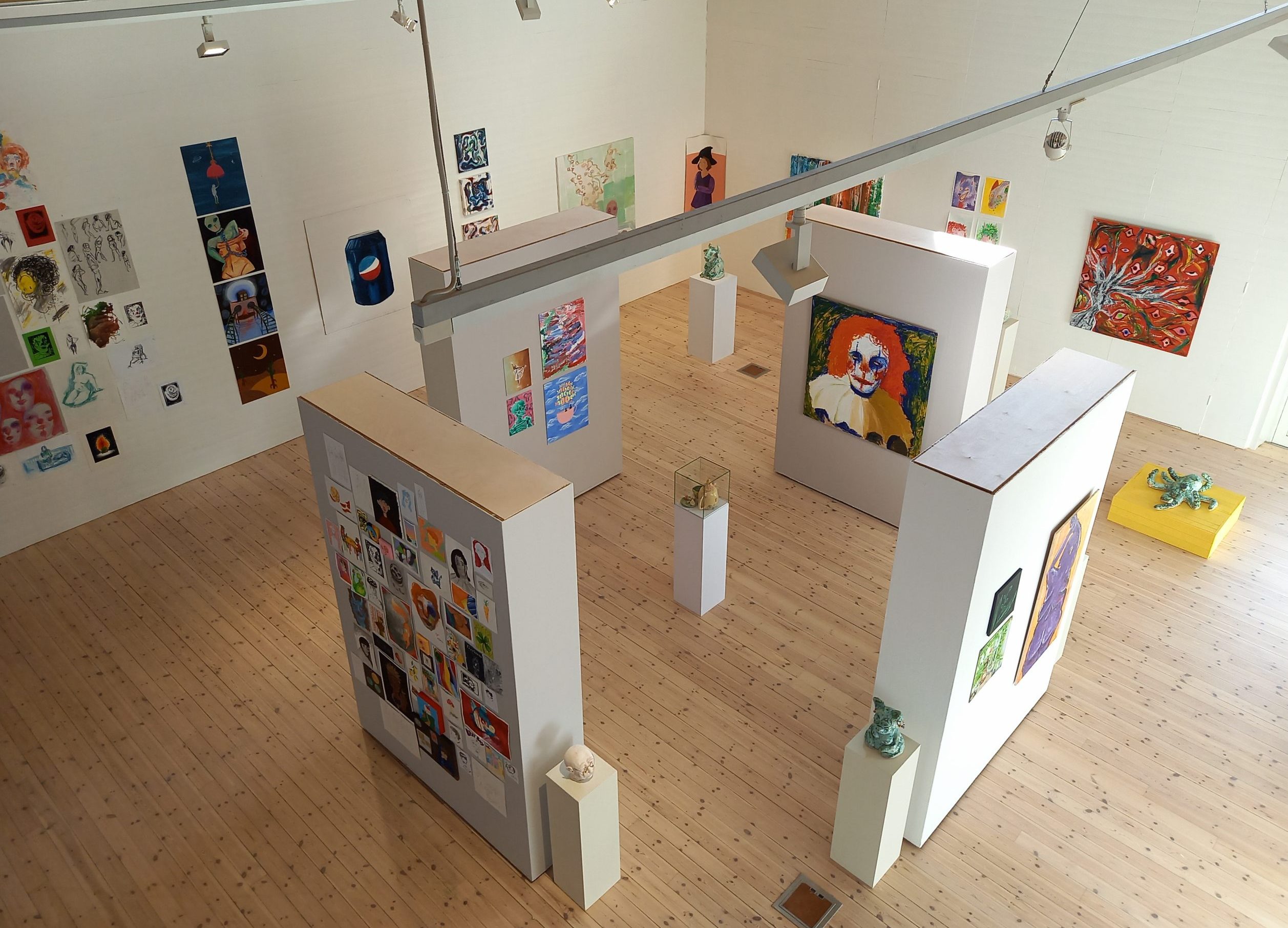 Foto. Överblick av utställningsrummet som fyllts av färgrik och variationsrik konst, främst målningar men även sex skulpturer går att se.