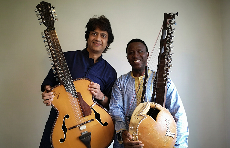 Foto. Manishe Pingle till vänster bredvid Lamine Cissokho till höger. Båda håller sina instrument, ler och tittar in i kameran