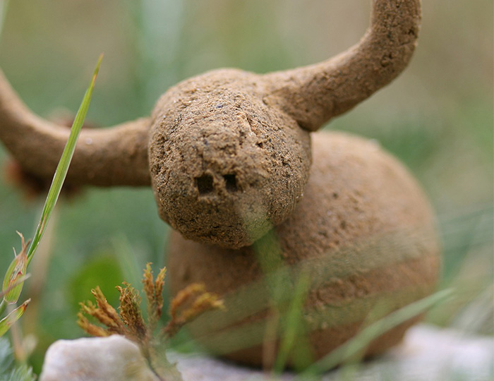 En närbild på en liten buffel gjord i lera som står i gräset.