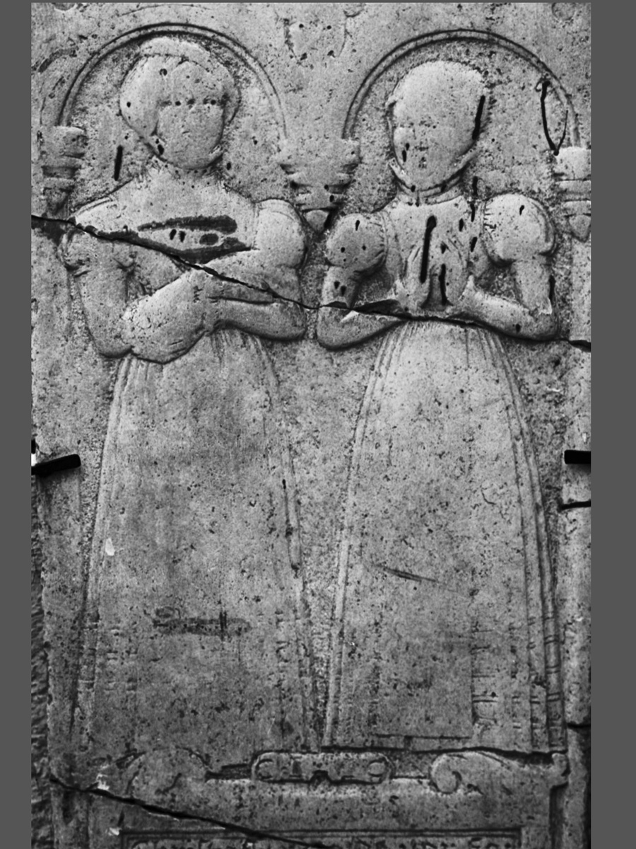 Skulpterad gravhäll med två unga kvinnor i långa dräkter. Hällen är sliten.