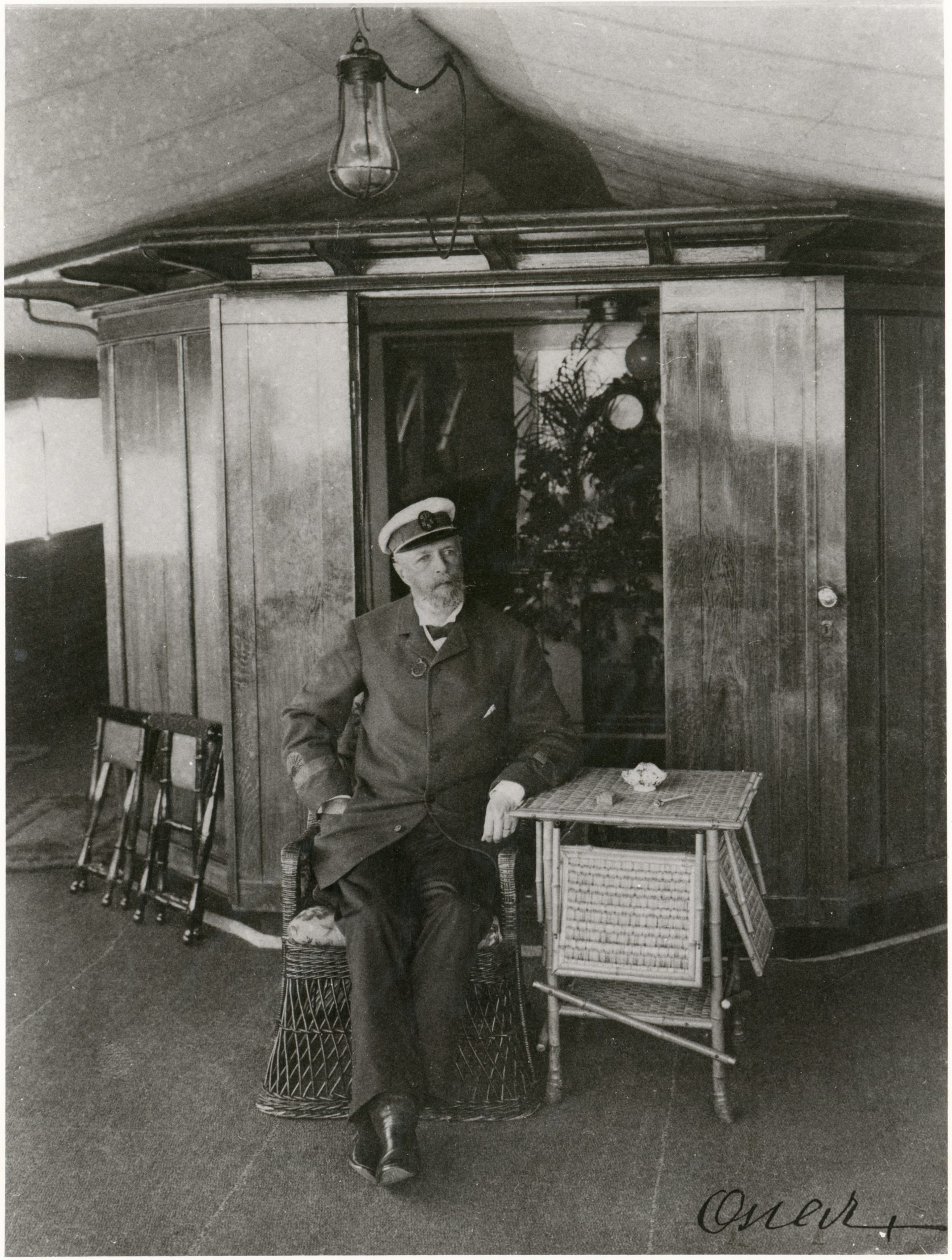 Svartvitt foto av kung Oscar II sittande ombord på en båt.