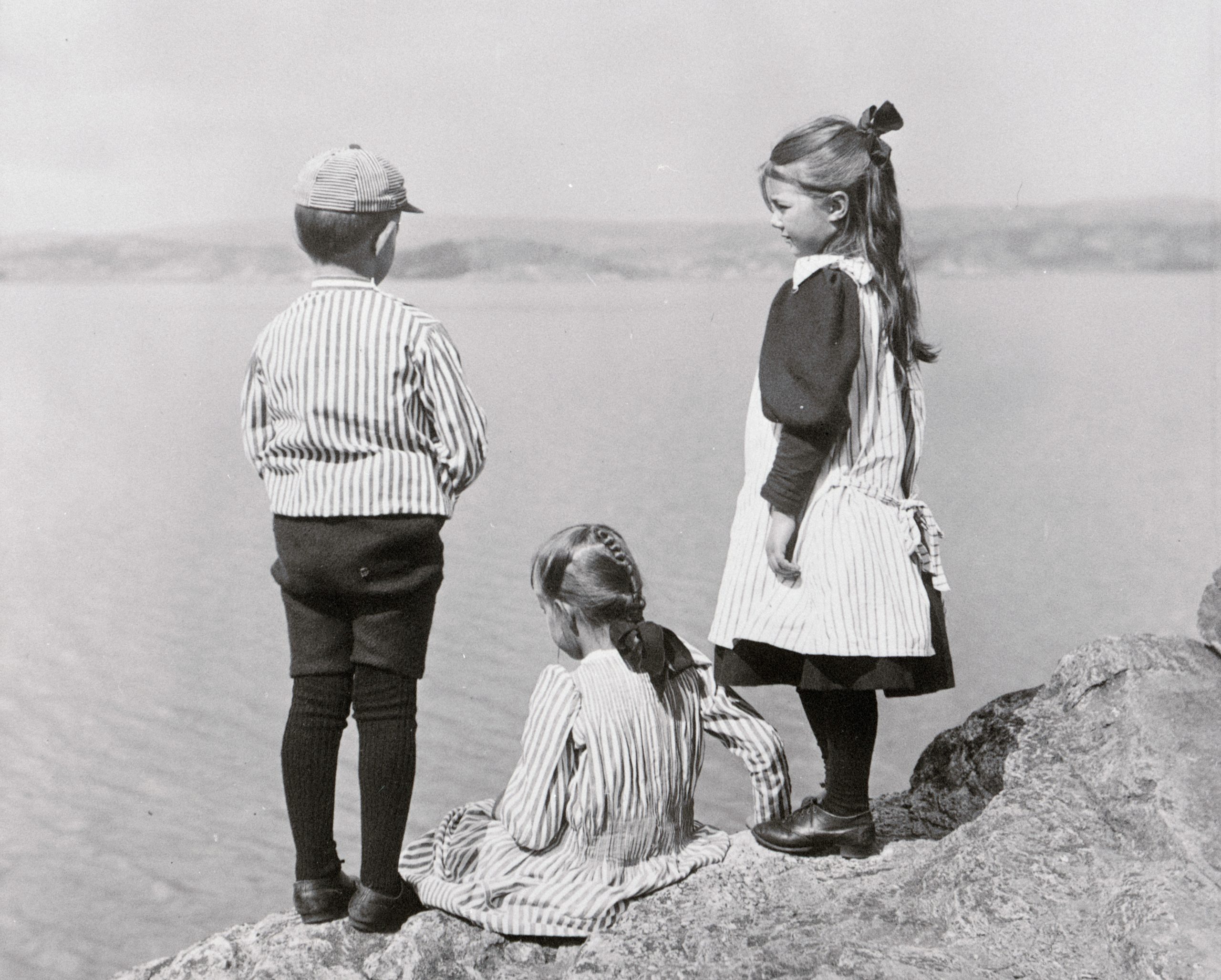 Svartvitt foto. Tre barn i fem till sjuårsåldern tittar ut över havet.