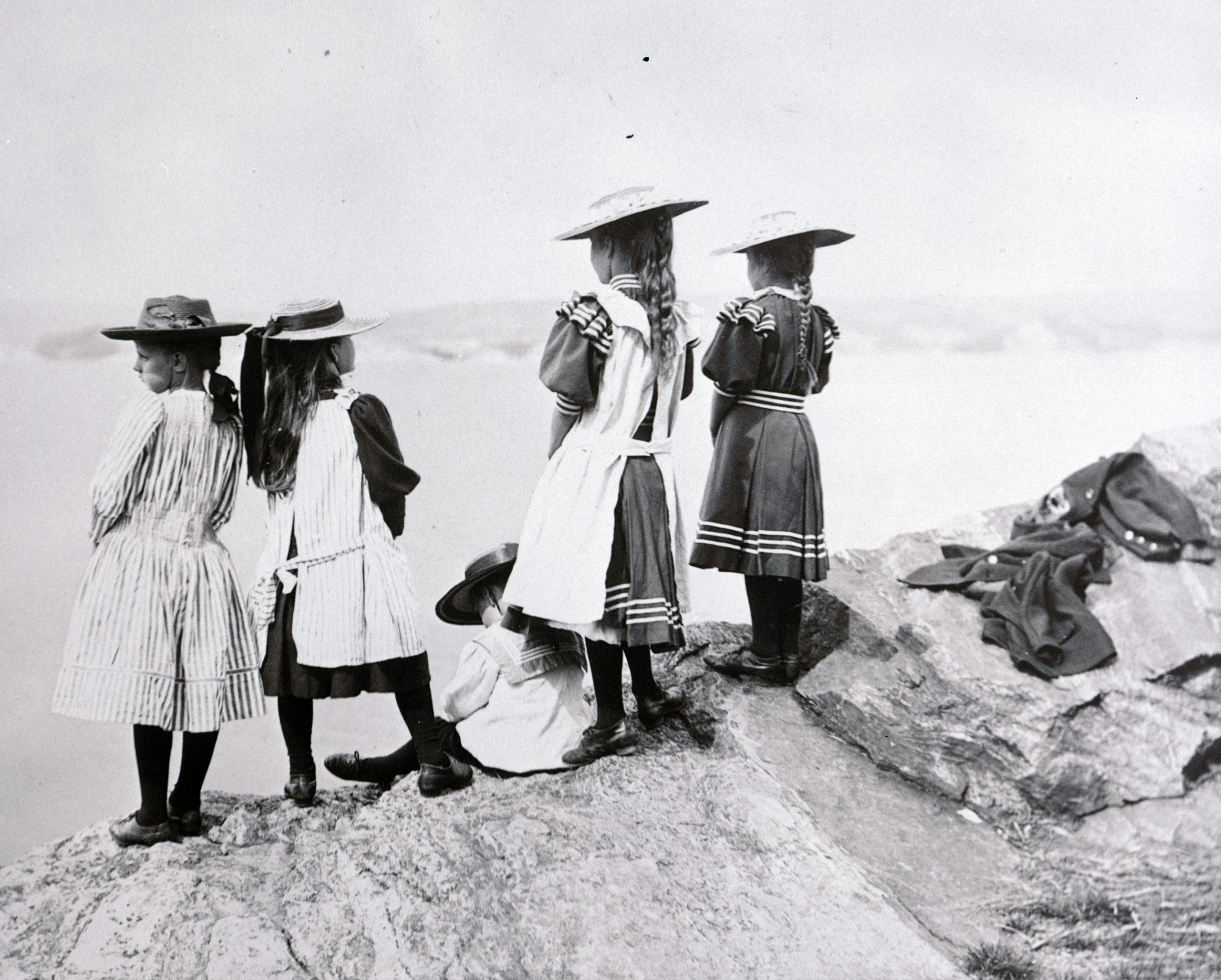 Svarvitt foto. Fyra flickor i stråhattar blickar ut över havet.