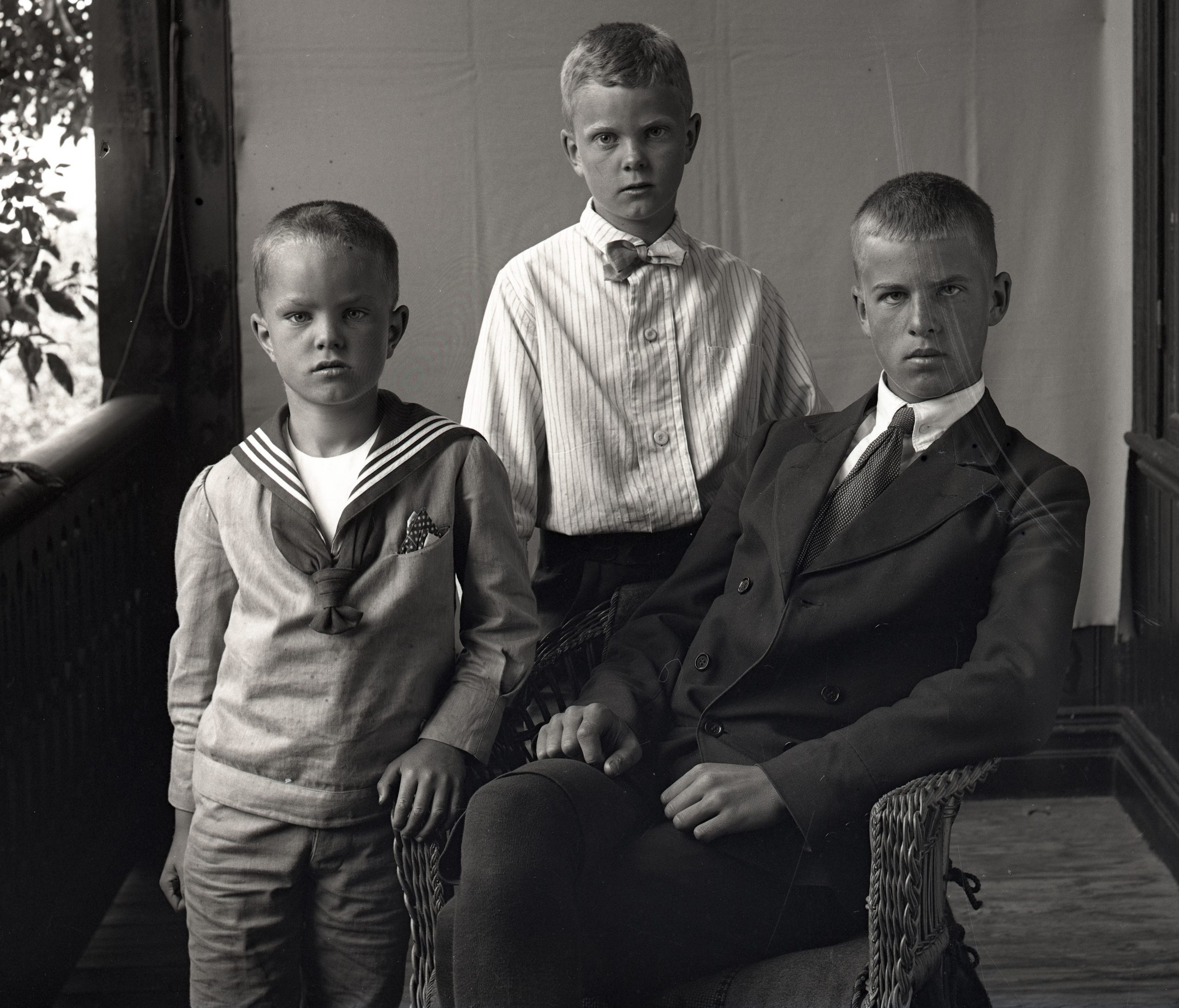 Svartvitt foto. Gruppbild med tre pojkar på en veranda.