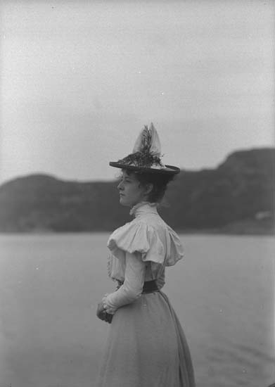 Svartvitt foto. Halvbild i profil av ung kvinna i hatt som tittar ut över havet.