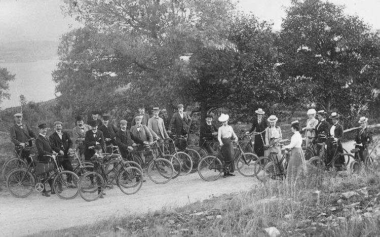 Svartvitt foto. Gruppbild med ett tjugofemtal kvinnor och män som står vid sina cyklar.
