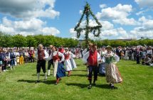 midsommarstång med personer som dansar runt i folkdräkter