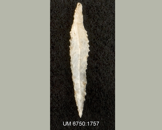 Foto som visar ett vitt, långsmalt rombiskt föremål i flinta. Övre delen är trubbig och nedre delen är spetsig. Föremålets långsidor har taggiga kanter.