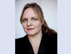 Porträttfoto. Isabell Schierenbeck, tittar in i kameran med ett svagt leende. Uppsatt blont hår i tofs.