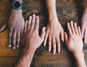 Foto. Fem händer som möts på ett bord, olika hudfärger.