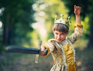 Foto. Ett barn utklädd till prinsessa. Håller ett svärd som hon riktar snett mot kameran hon tittar i svärdets riktning.