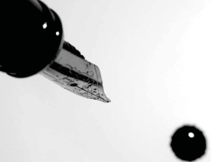Foto. En penna med bläckstift som droppar bläck på ett vitt papper.