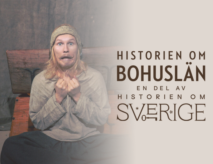 Foto. Man tittar sitter framför en träkista och tittar in i kameran med öppen mun och ögonen uppspärrade. Kläder i vikingastil.