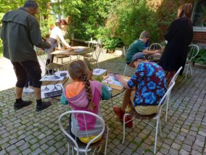 En grupp unga personer som sitter och tecknar och målar utomhus.
