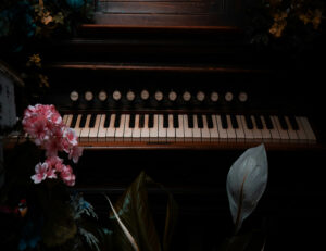 Foto. Piano och i förgrunden blommor.
