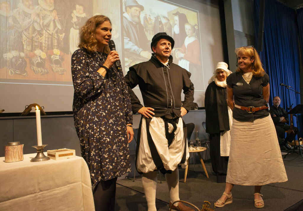 Foto. Tre kvinnor och en man på en scen. Två av personerna bär historiska dräkter.