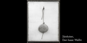 Svartvitt foto. En rund sten, karvad i mitten upphängd i ett snöre mot vit bakgrund.