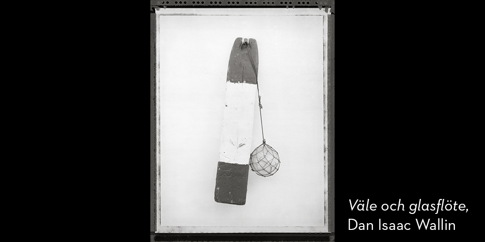 Svartvitt foto. En träbit målad i mörkare färg i ändarna och vit färg i mitten med ett sfäriskt glassänke fäst i rep.