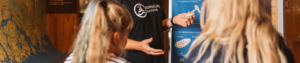 Foto. Tre personer står samlade i en cirkel. Två flickor och en man arbetande på Bohusläns museum som berättar om utställningarna.