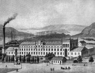 Foto. Svartvit. På bilden visas en överskådlig bild över Uddevallas hamn och Kampenhofs industribyggnad.