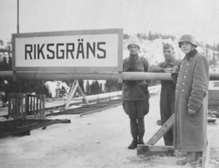 Svartvitt foto. Tre män som står bredvid varandra nära en skylt med texten: Riksgräns.